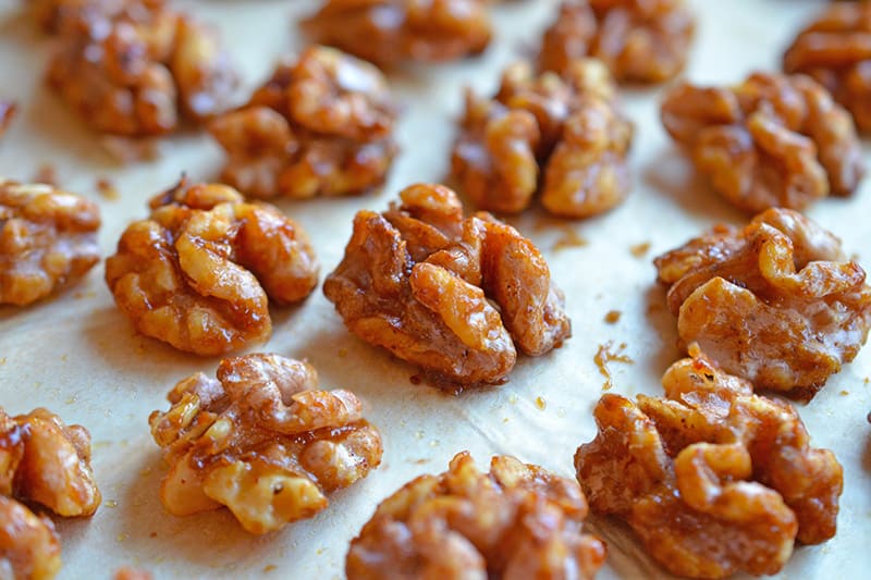 Close up of the sweetened gluten-free walnuts baking on a piece of parchment paper. 