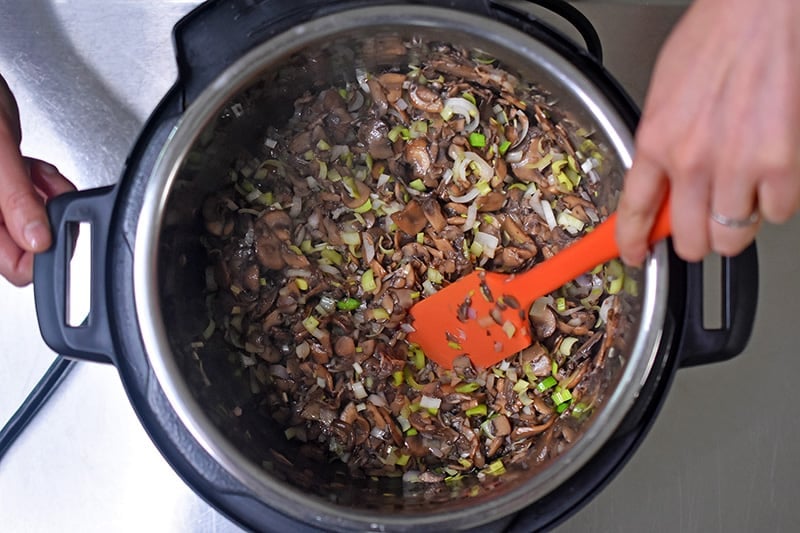 Someone mixing the mushrooms, leeks, and shallots in an Instant pot for Instant Pot cream of mushroom soup.