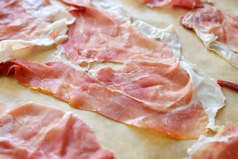 Slices of prosciutto on a baking sheet.