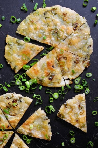 An overhead shot to two Paleo Scallion Pancakes cut into wedges and surrounded by sliced scallions.
