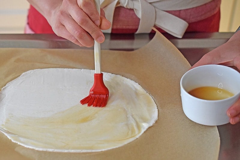 Brushing sesame oil on a flattened piece of cassava flour dough to make vegan and paleo scallion pancakes
