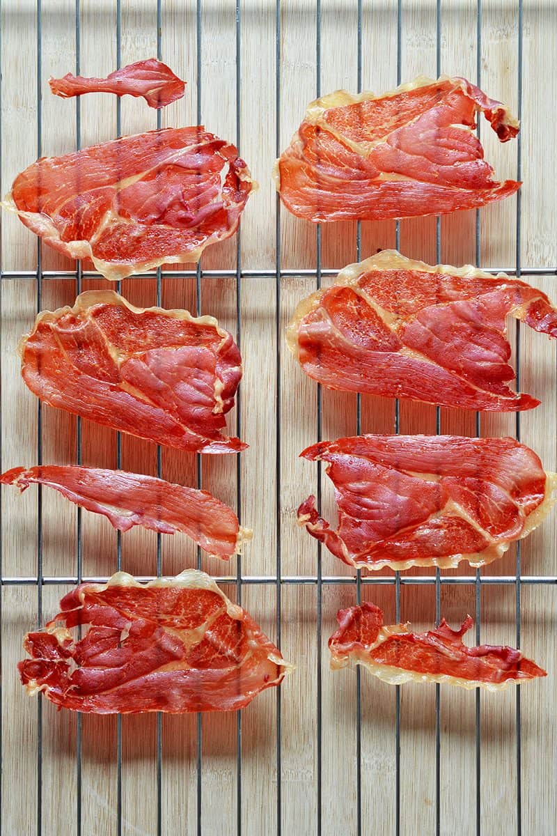 Baked slices of prosiutto on a wire rack.