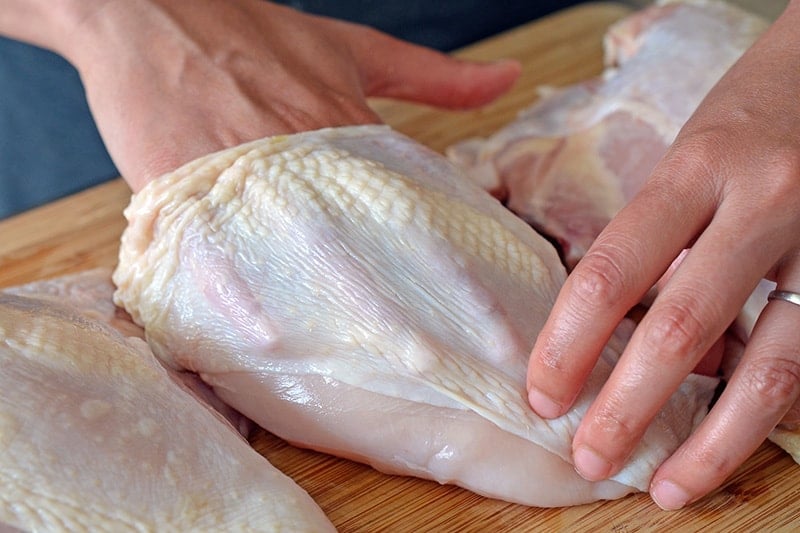 Loosening the skin between the chicken skin and the breast with a hand.