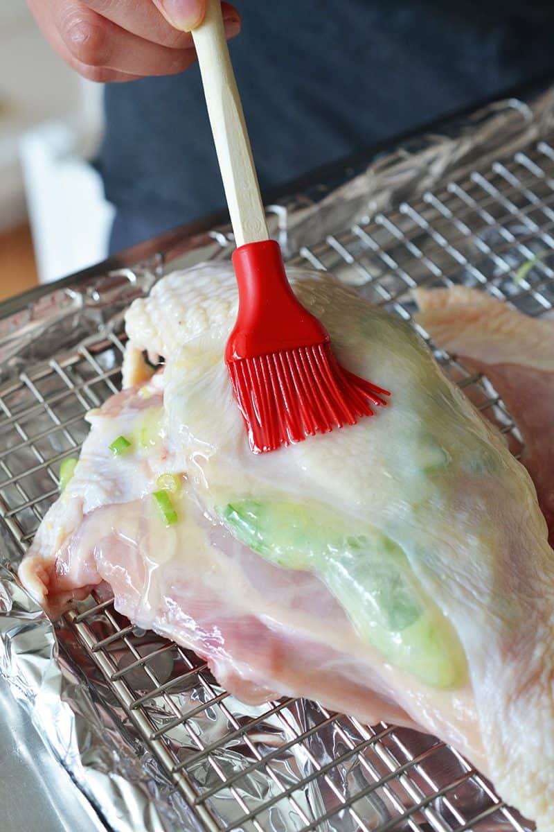 Melted fat is brushed on top of the Ginger-Scallion Chicken with a red silicone brush.
