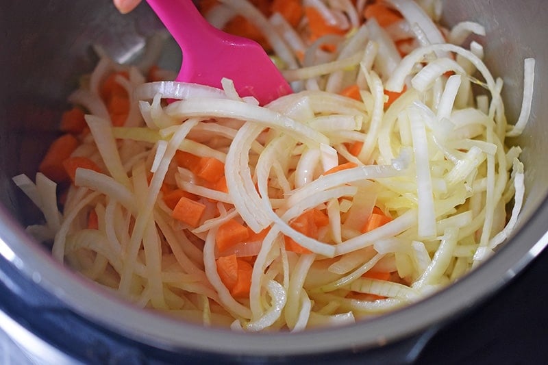 A closeup of diced carrots and sliced onions being sautéed in an open Instant Pot.