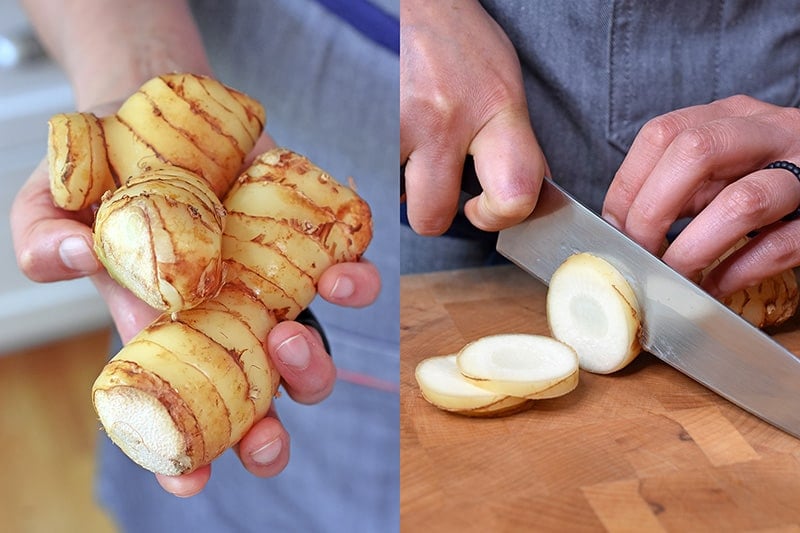 Fresh galangal being held in a hand and being sliced on a cutting board.