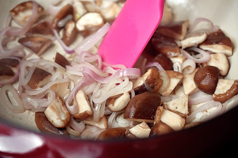 Sautéing sliced shallots and quartered shiitake mushrooms in a pot to make healthy Tom Kha Gai