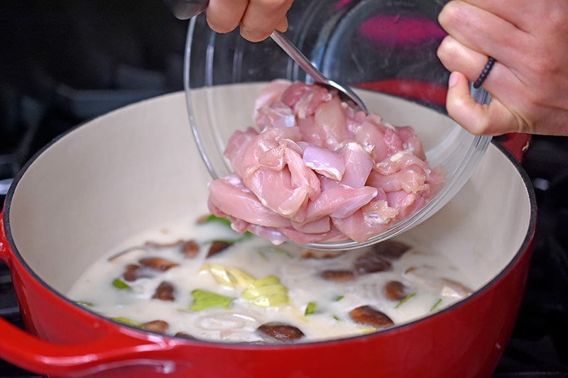 Adding sliced chicken to a simmering pot of homemade keto Tom Kha Gai 