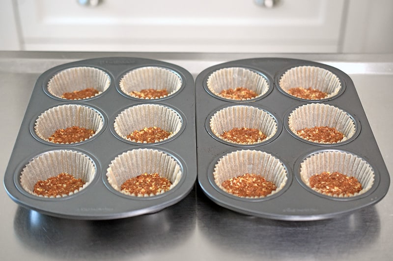 A shot of muffin tins filled with parchment cups and No-Bake Matcha Cheesecake crust on the bottom.