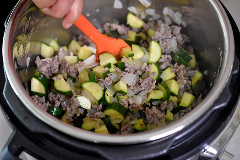 An overhead shot of someone stirring Instant Pot Zucchini Bolognese in an open Instant Pot.