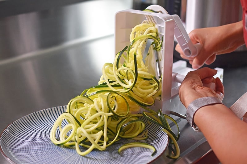 A person is cranking a spiralizer to make zucchini noodles.