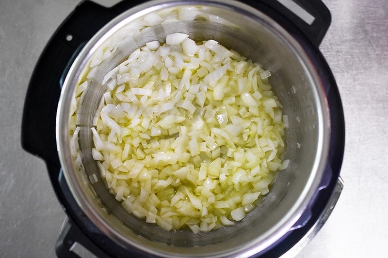 An overhead shot of diced onions sautéing in olive oil in an open Instant Pot.
