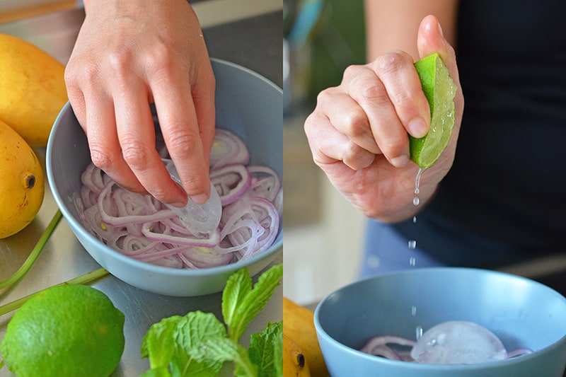 Sliced red onions in a bowl with someone squeezing fresh lime juice into the bowl.