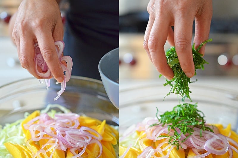 Someone adding sliced onions and mint into a bowl containing ingredients for spicy mango cabbage slaw.