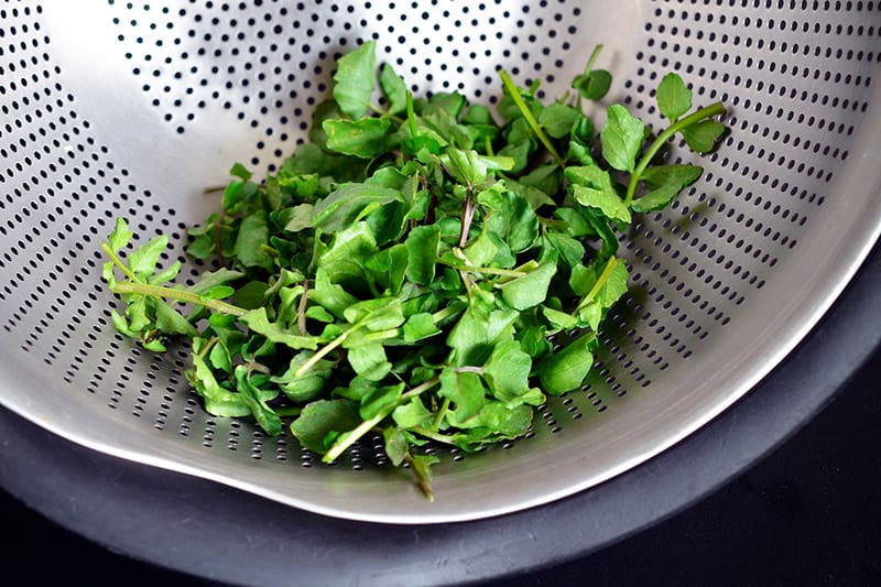 Watercress sitting in a colander.
