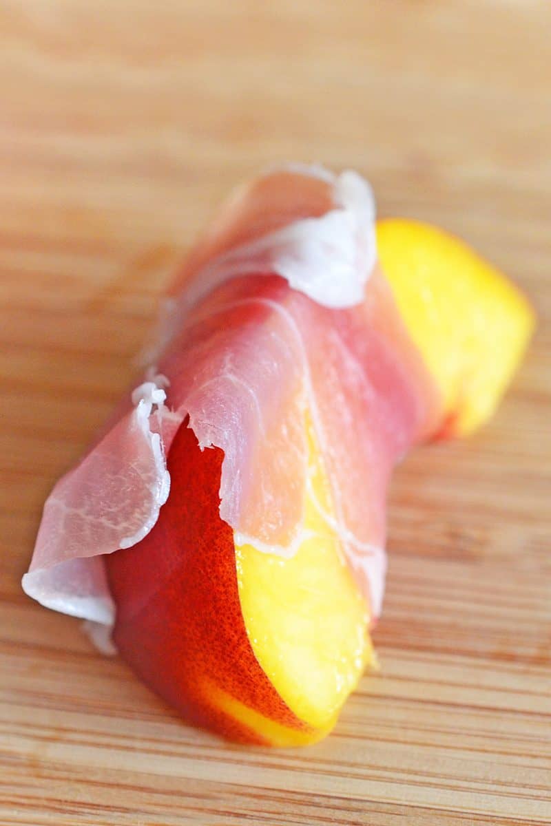 A close-up shot of a slice of peach wrapped with a thin slice of prosciutto.