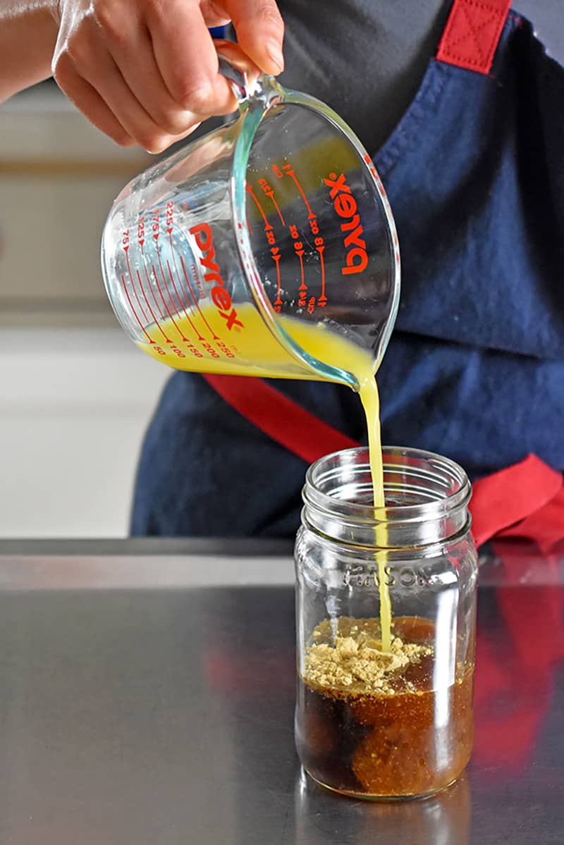 Pouring orange juice into a jar filled with All-Purpose Stir-Fry Sauce ingredients 