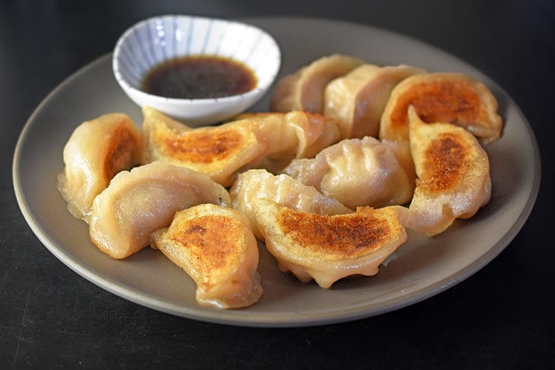 A close up of Paleo Pot Stickers with crispy golden bottoms and a dish of dipping sauce in the background.