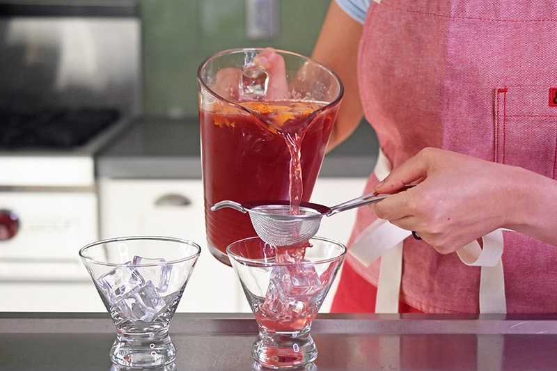 The Pomegranate Orange Mocktail is poured from the pitcher. The mocktail is poured through a strainer into a cocktail glass filled with ice.