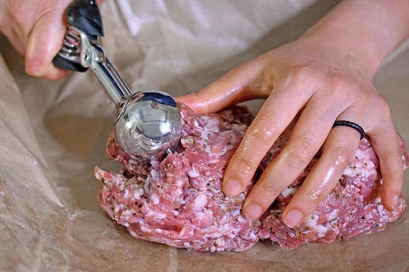 Two hands are shown scooping bulk Italian sausage with a medium sized disher.