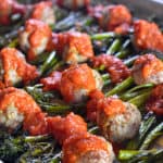 Diagonal shot of Sheet Pan Meatballs and Broccolini supper topped with marinara sauce.