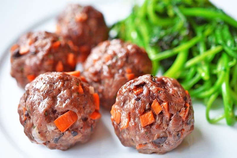 A plate is filled with gluten-free and paleo Asian Meatballs and stir-fried spinach.