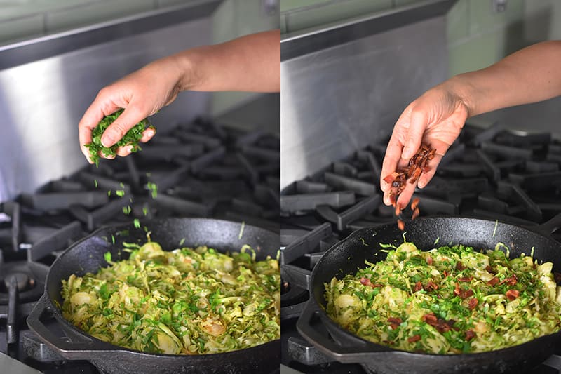 A hand is sprinkling fresh herbs and crispy bacon bits on top of the shaved Brussels sprouts.