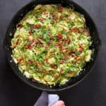 An overhead shot of shaved Brussels sprouts with bacon in a large cast iron skillet.