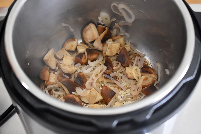 An overhead shot of an open Instant Pot with cooked shallots and shiitake mushrooms.
