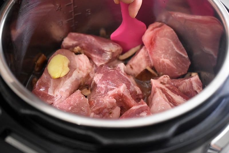 A closeup of the inside of an Instant Pot where someone is stirring the contents with a silicone spatula.