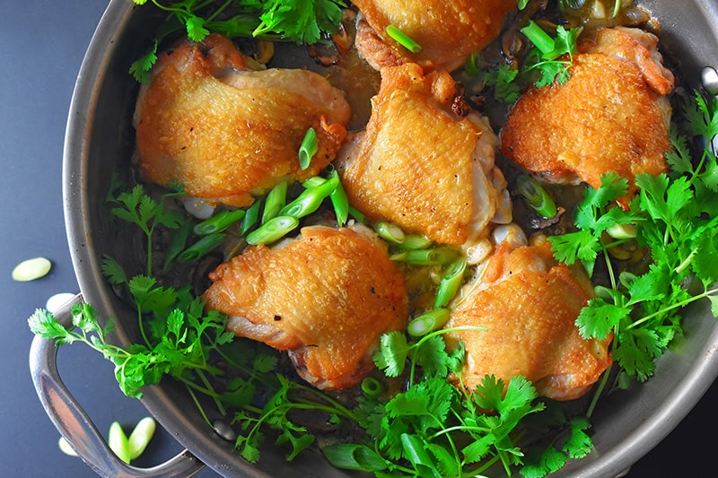 An overhead shot of Cantonese Crispy Chicken Thighs in a skillet surrounded with fresh cilantro and scallions.