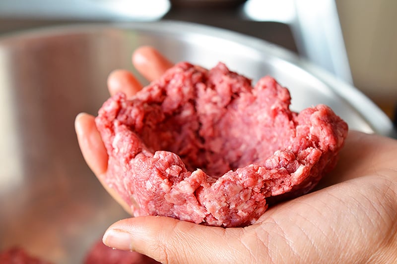 A hand holding some raw ground beef that has been formed into a bowl shape.