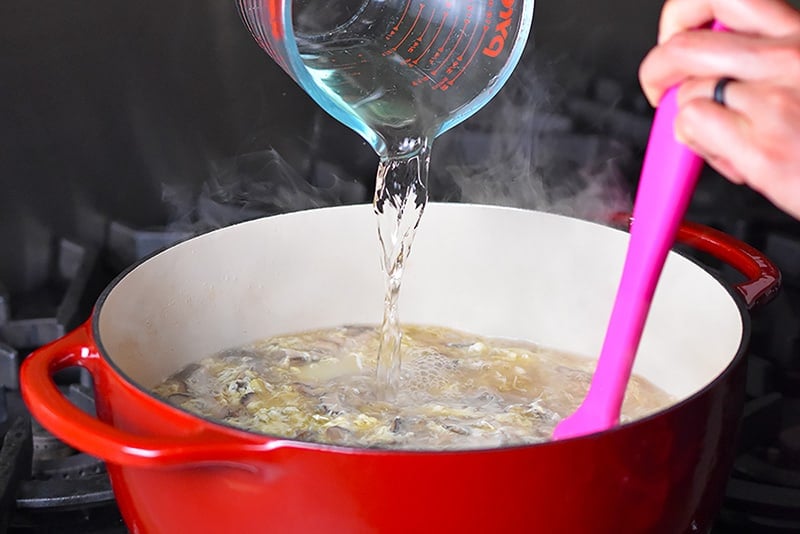 Pouring rice vinegar into the Hot and Sour Soup off the heat.