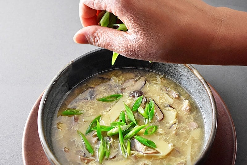 Garnishing a bowl of hot and sour soup with sliced scallions