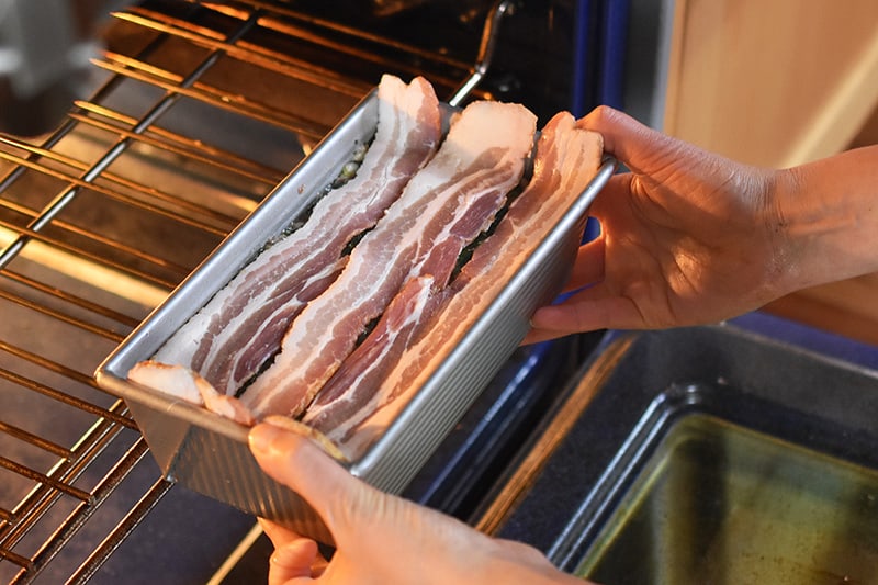 Placing the bacon-topped meatloaf into the oven.