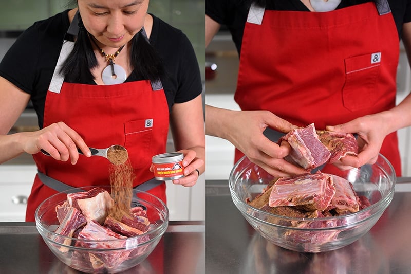A woman is adding a tablespoon of Magic Mushroom Powder to a bowl filled with short ribs. She uses her hands to toss them together.