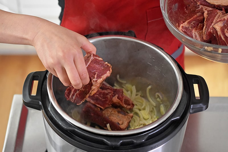 The seasoned short ribs are added to the Instant Pot filled with sliced shallots and garlic.