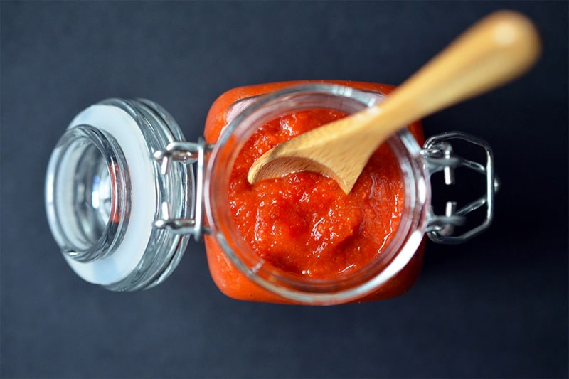 An overhead shot of a jar filled with homemade Whole30 sriracha with a wooden spoon inside.