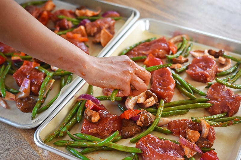 Dividing the pork and vegetables onto two parchment-lined rimmed baking sheets.