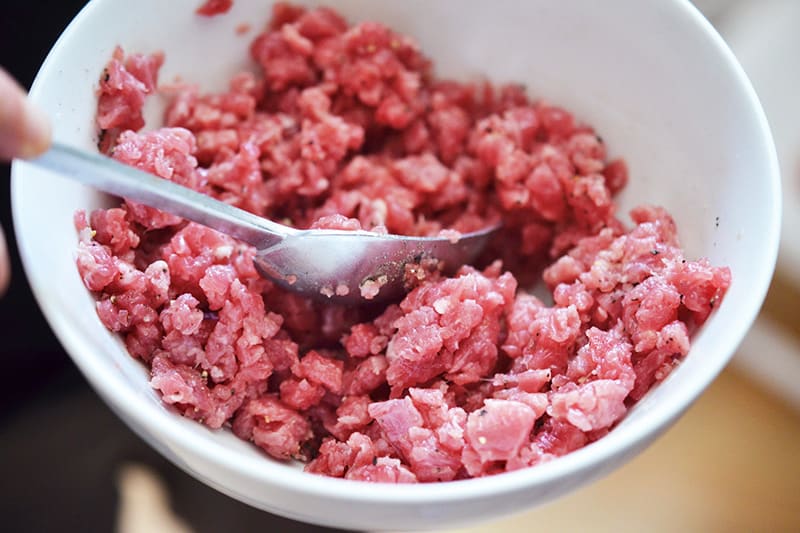 A white bowl filled with minced raw beef with seasonings