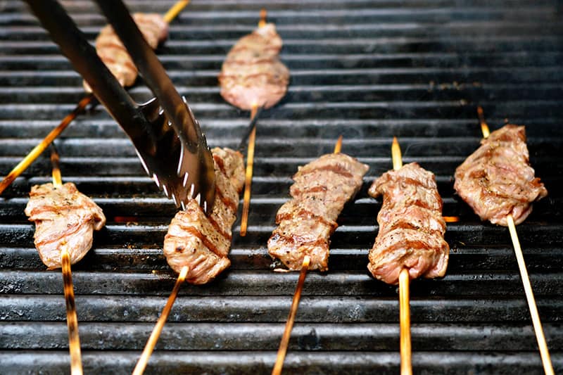 Fully cooked Whole30-friendly smashed steak skewers are removed from the grill with tongs.
