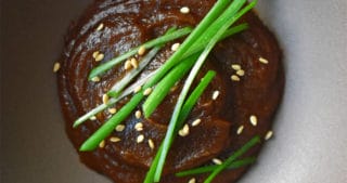 An overhead shot of a dish filled with paleo hoisin sauce topped with sesame seeds and chives