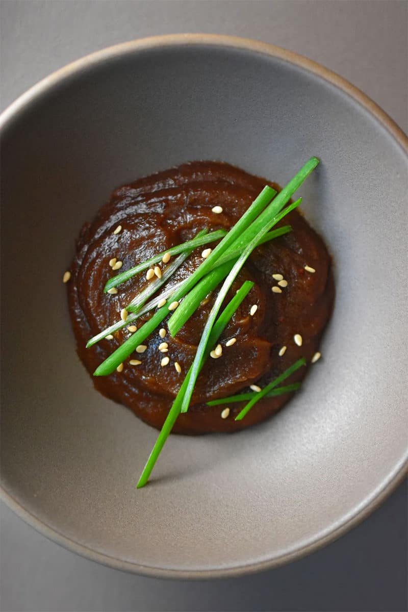 An overhead shot of paleo hoisin sauce in a gray bowl topped with sesame seeds and chives