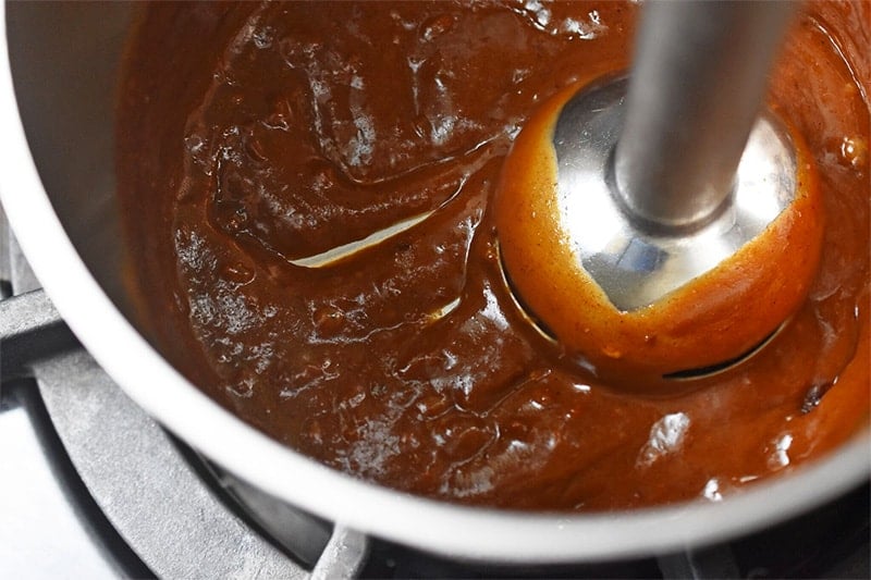 An overhead shot of an immersion blender blending homemade paleo hoisin sauce in a small saucepan.