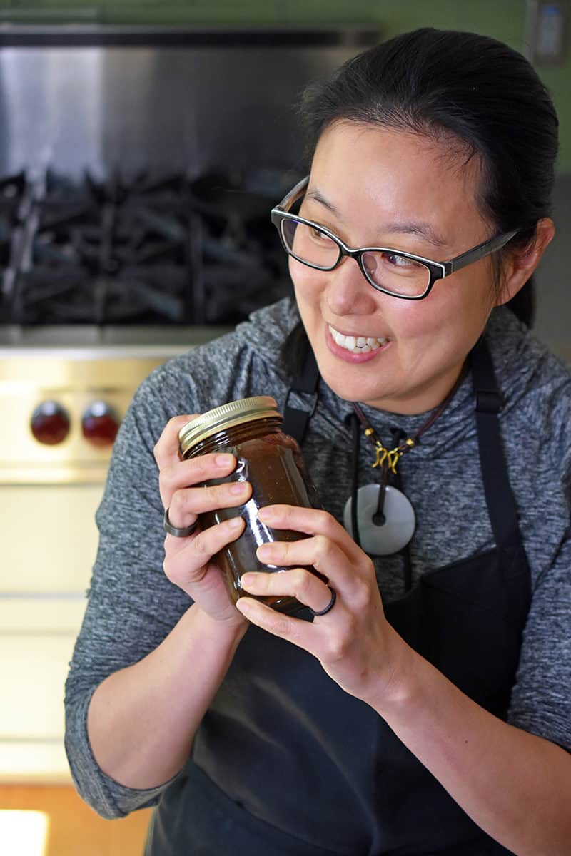 A shot of a smiling woman shaking a jar of All-Purpose Stir-Fry Sauce.
