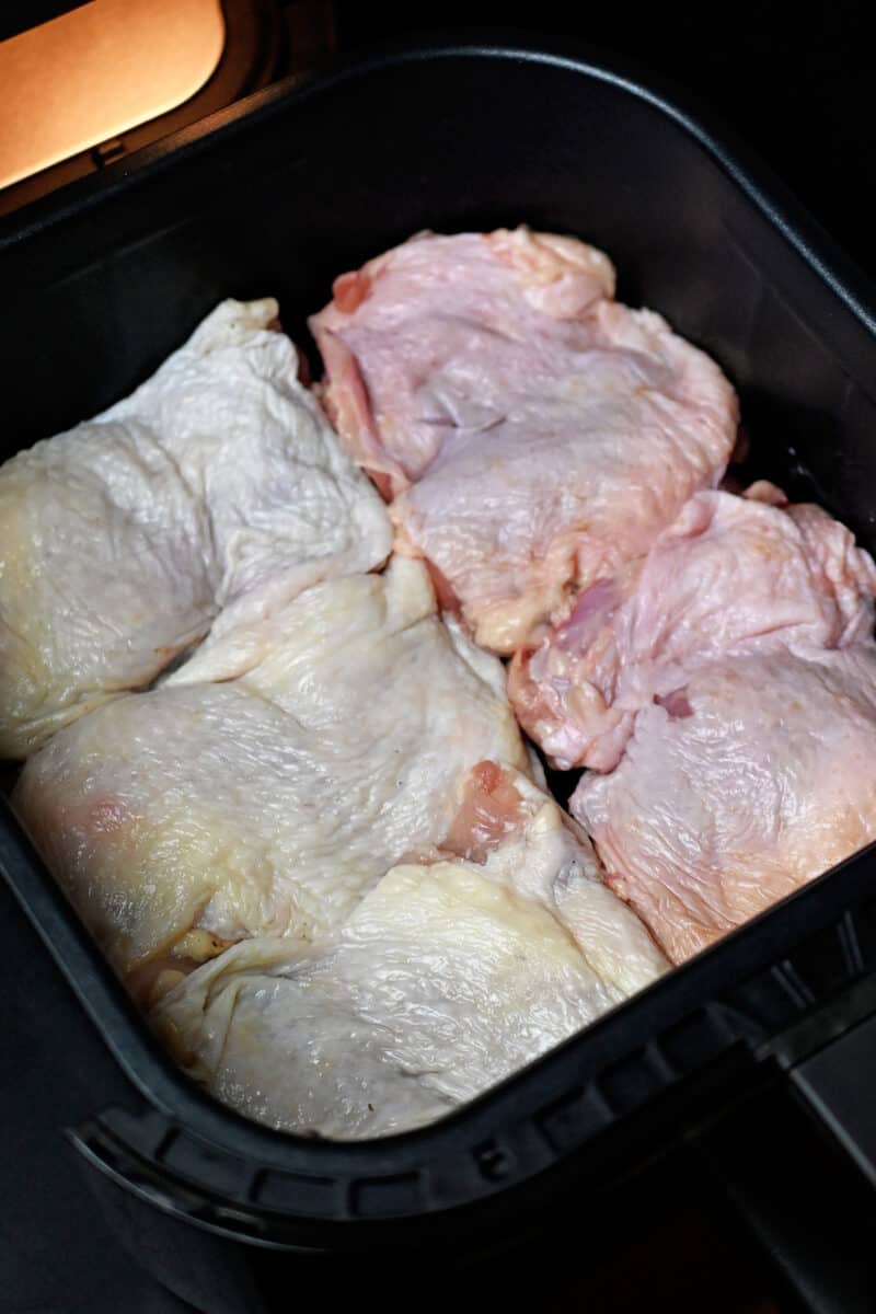 An overhead shot of five raw chicken thighs in a single layer in an air fryer basket.