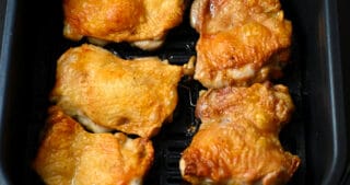 An overhead shot of crispy air fryer chicken thighs in an open air fryer basket.
