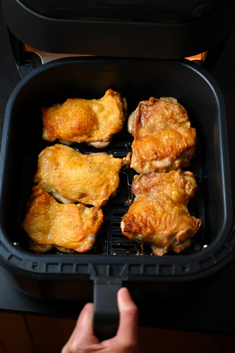 An overhead shot of crispy air fryer chicken thighs in an open air fryer basket.