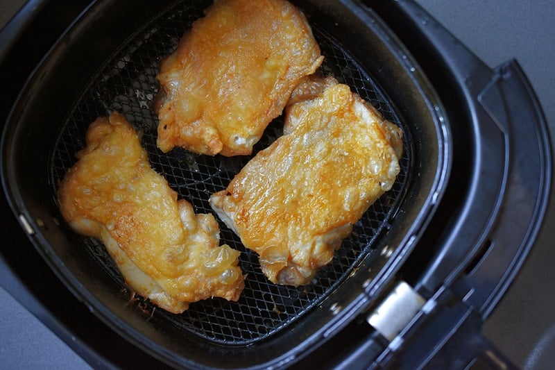 An overhead shot of three Air Fryer Cracklin’ Chicken thighs ready to eat in an air fryer basket.
