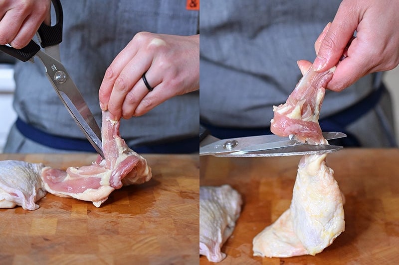 A person is removing the bone from a skin-on chicken thigh with a pair of kitchen shears.